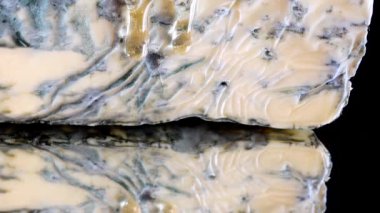 Dorblu peynirinden akmakta olan bal damlaları aynalı siyah arka planda.