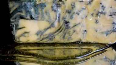 Dorblu peynirinden akmakta olan bal damlaları aynalı siyah arka planda.