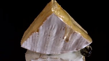 Brie peynirinden damlayan bal damlaları aynalı siyah arka planda.