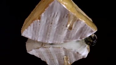 Brie peynirinden damlayan bal damlaları aynalı siyah arka planda.