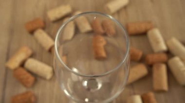 Şarap, şarap mantarlarının arka planındaki bir bardağa dökülür..