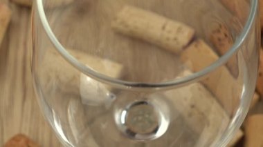 Şarap, şarap mantarlarının arka planındaki bir bardağa dökülür..