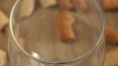 Şarap, şarap mantarlarının arka planındaki bir bardağa dökülür..