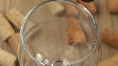 Şarap, şarap mantarlarının arka planındaki bir bardağa dökülür..