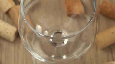 Şarap, şarap mantarlarının arka planındaki bir bardağa dökülür..