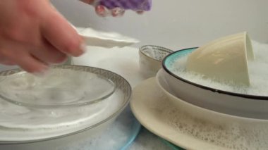 Bir kadın sabunlu bir bez ile bulaşıkları yıkıyor..