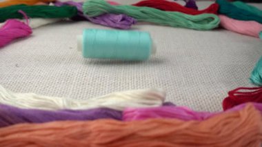 Renkli küf ipliklerinin arka planına karşı çuval bezi üzerine çok renkli makaralar dökülüyor. Yavaş çekim.