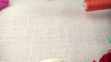Renkli küf ipliklerinin arka planına karşı çuval bezi üzerine çok renkli makaralar dökülüyor. Yavaş çekim.