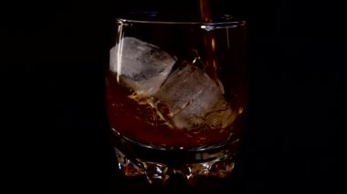 İzole edilmiş siyah arka planda buzlu bir bardağa viski dökmek. Yavaş çekim.