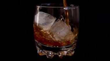 İzole edilmiş siyah arka planda buzlu bir bardağa viski dökmek. Yavaş çekim.