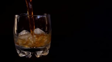 İzole edilmiş siyah arka planda buzlu bir bardağa viski dökmek. Yavaş çekim.