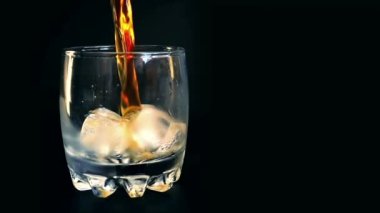 İzole edilmiş siyah arka planda buzlu bir bardağa viski dökmek. Yavaş çekim.