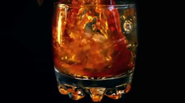 İzole edilmiş siyah arka planda buzlu bir bardağa viski dökmek. Yavaş çekim.