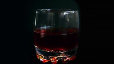 İzole edilmiş siyah arka planda buzları viski bardağına düşürmek. Yavaş çekim.