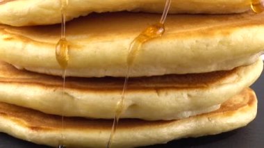 Beyaz arka planda akçaağaç pekmezli Amerikan gözlemeleri. Krep siyah, yuvarlak bir taşın üzerinde yatıyor..