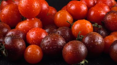 Su damlalarında siyah arkaplanda vişne domatesleri.