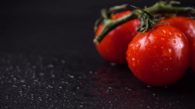 Su damlalarında siyah arkaplanda vişne domatesleri.