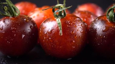 Su damlalarında siyah arkaplanda vişne domatesleri.