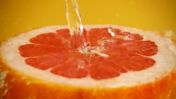 Een Halve Grapefruit Een Straal Water Een Oranje Achtergrond Langzame — Stockvideo