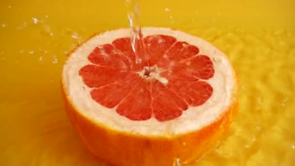 オレンジの背景に水のジェットでグレープフルーツの半分 スローモーション — ストック動画