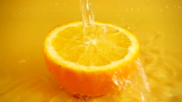 Eine Halbe Orange Einem Wasserstrahl Auf Orangefarbenem Hintergrund Zeitlupe — Stockvideo