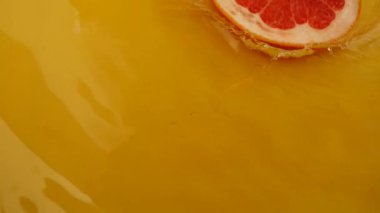 Greyfurt dilimleri turuncu arka planda suya düşer. Yavaş çekim.