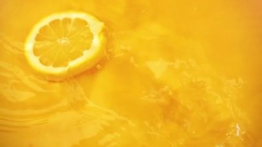 Limon dilimleri turuncu arka planda suya düşer. Yavaş çekim.