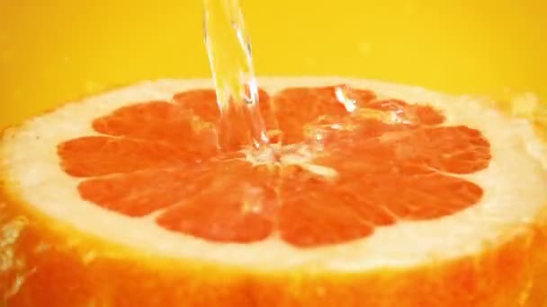 オレンジの背景に水のジェットでグレープフルーツの半分 スローモーション — ストック動画