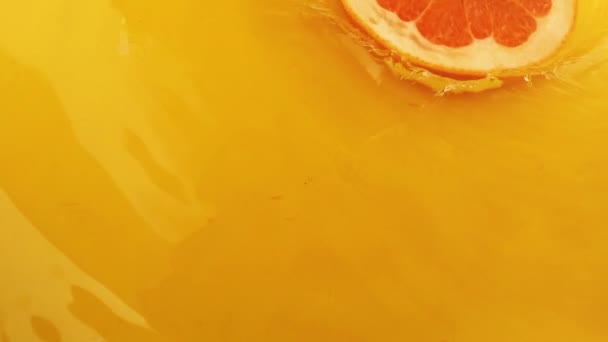グレープフルーツのスライスはオレンジの背景に水に落ちる スローモーション — ストック動画