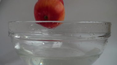 Falling apples in a glass bowl of water. Slow motion.