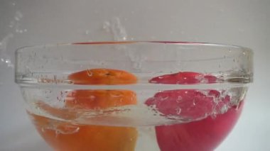 Portakal, limon ve elmayı cam bir kase suya döküyorum. Yavaş çekim.