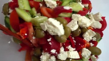 Preparing a salad in a glass bowl of lettuce, tomatoes, cucumbers, sweet peppers, olives and bryndza and feta cheese.