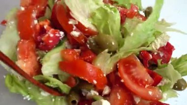 Preparing a salad in a glass bowl of lettuce, tomatoes, cucumbers, sweet peppers, olives and bryndza and feta cheese.