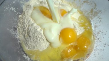 Cam bir kasede hamur pişirmek. İçinde un ve yumurta olan bir kaseye süt dökülüyor. Yavaş çekim.