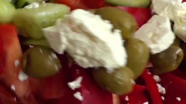 Preparing a salad in a glass bowl of lettuce, tomatoes, cucumbers, sweet peppers, olives and bryndza and feta cheese.