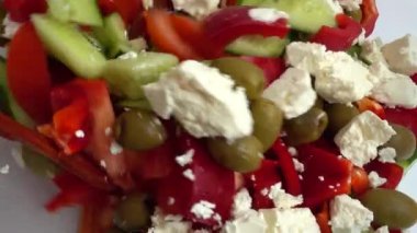Preparing a salad in a glass bowl of lettuce, tomatoes, cucumbers, sweet peppers, olives and bryndza and feta cheese.