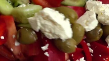 Preparing a salad in a glass bowl of lettuce, tomatoes, cucumbers, sweet peppers, olives and bryndza and feta cheese.