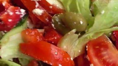 Preparing a salad in a glass bowl of lettuce, tomatoes, cucumbers, sweet peppers, olives and bryndza and feta cheese.