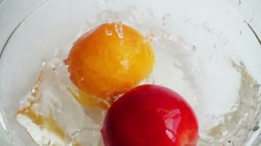 Falling orange, lemon and apple into a glass bowl of water. Slow motion.