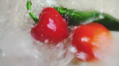 Domates, salatalık ve tatlı kırmızı biber cam bir kase suya düşer. Yavaş çekim.