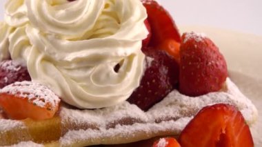 Çilekli Belçika waffleları, krema ve pudra şekerli beyaz bir arka planda..