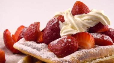 Çilekli Belçika waffleları, krema ve pudra şekerli beyaz bir arka planda..