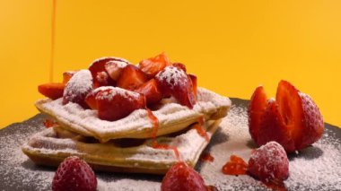 Çilekli Belçika waffleları, tatlı çilek sosu ve turuncu arka plandaki taş bir tahtada pudra şekeri..