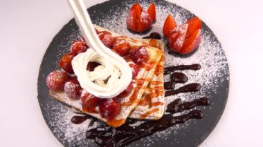 Çilekli Belçika waffleları, tatlı çilek soslu, krem şantili ve pudra şekerli beyaz arka planda bir taş tahtada.