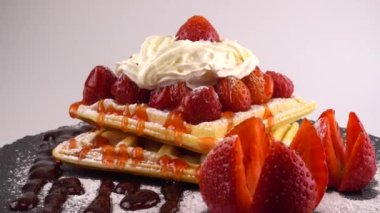 Çilekli Belçika waffleları, tatlı çilek soslu, krem şantili ve pudra şekerli beyaz arka planda bir taş tahtada.