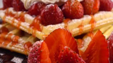 Çilekli Belçika waffleları, tatlı çilek soslu, krem şantili ve pudra şekerli beyaz arka planda bir taş tahtada.