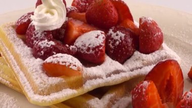 Çilekli Belçika waffleları, krema ve pudra şekerli beyaz bir arka planda..