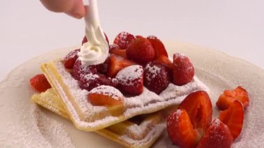 Çilekli Belçika waffleları, krema ve pudra şekerli beyaz bir arka planda..