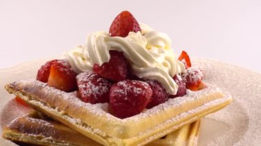 Çilekli Belçika waffleları, krema ve pudra şekerli beyaz bir arka planda..