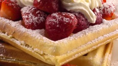 Çilekli Belçika waffleları, krema ve pudra şekerli beyaz bir arka planda..